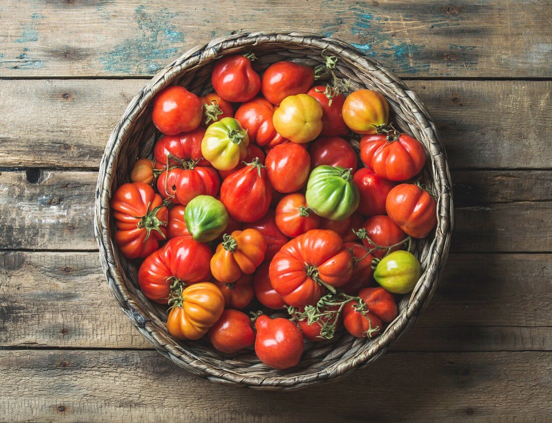 Bunte Heirloom-Tomaten im Korb auf Holzuntergrund