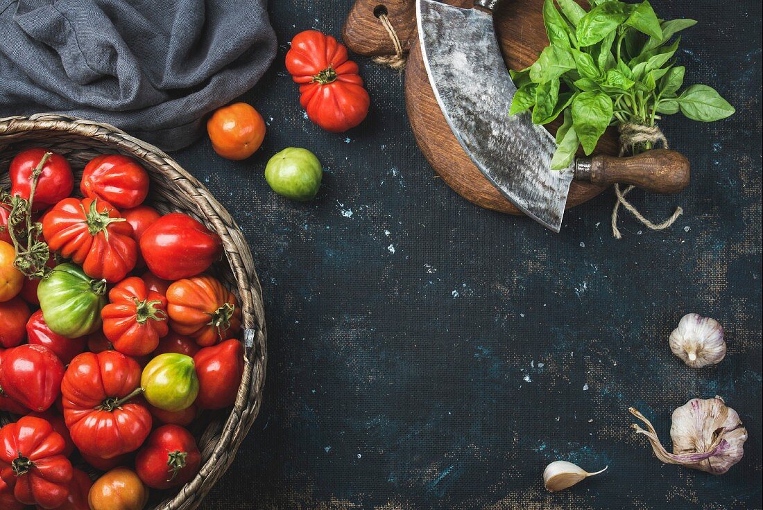 Bunte Heirloom-Tomaten im Korb, Basilikum, Knoblauch und Wiegemesser