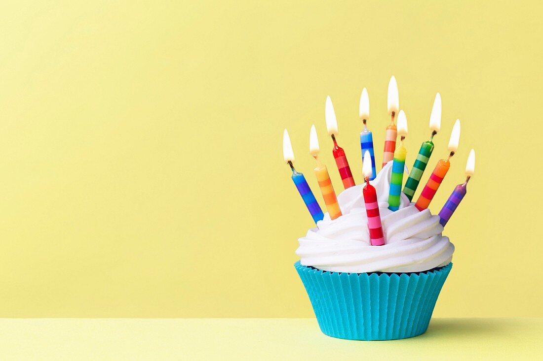 Geburtstags-Cupcake mit bunten Kerzen vor gelbem Hintergrund