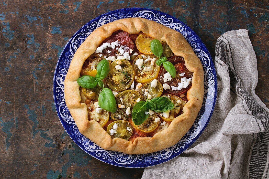 Homemade vegetable open pie galette with colorful tomatoes, tomato pesto, feta cheese and fresh basil