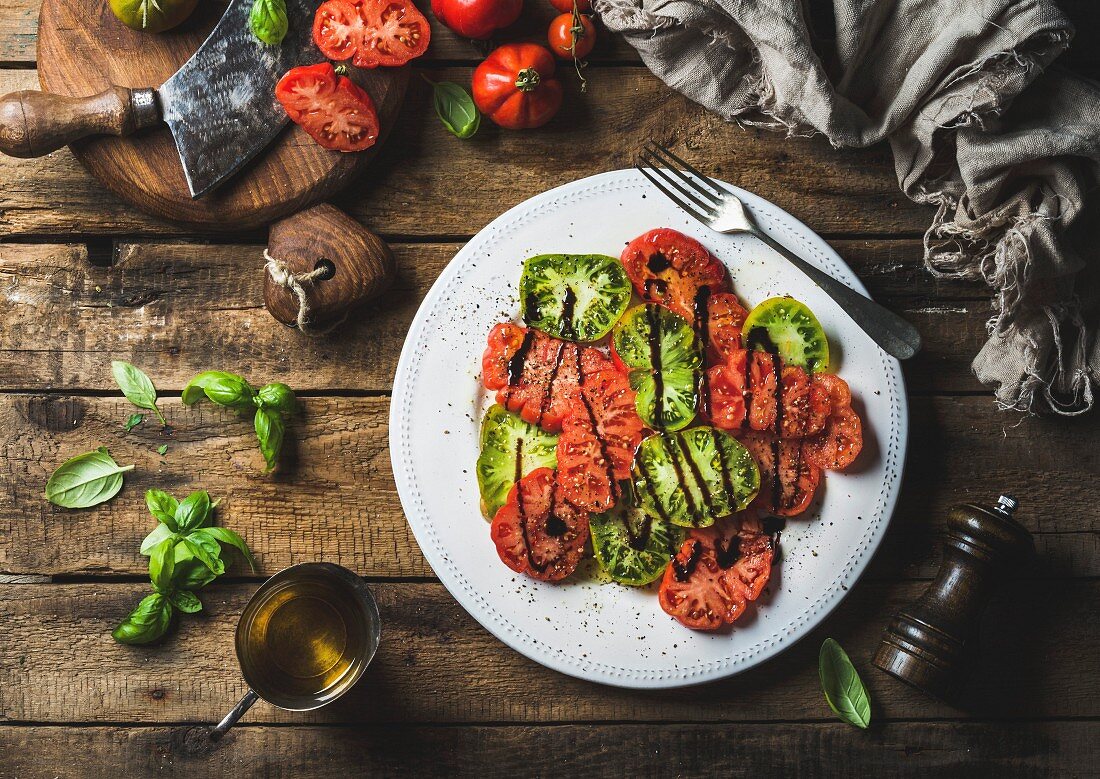 Heirloom tomato salad with olive oil, balsamic vinegar and basil over old rustic wooden background