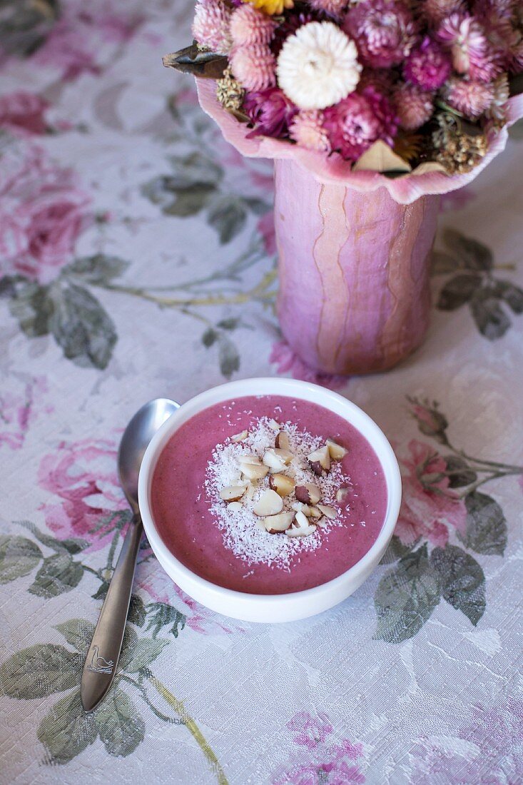 Raspberry smoothie bowl topped with coconut and chopped Brazil nuts on the table