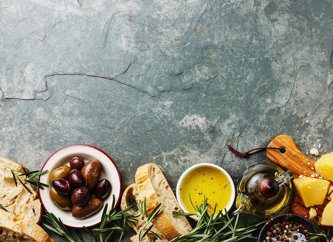 Italienische Zutaten: Ciabatta, Parmesan, Olivenöl, Oliven und Rosmarin auf grauem Steinuntergrund