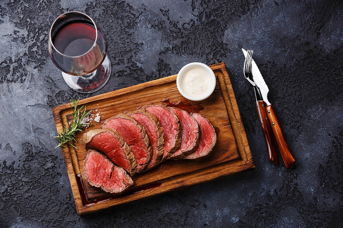 Sliced grilled tenderloin Steak roastbeef and Pepper sauce on wooden cutting board and Red wine