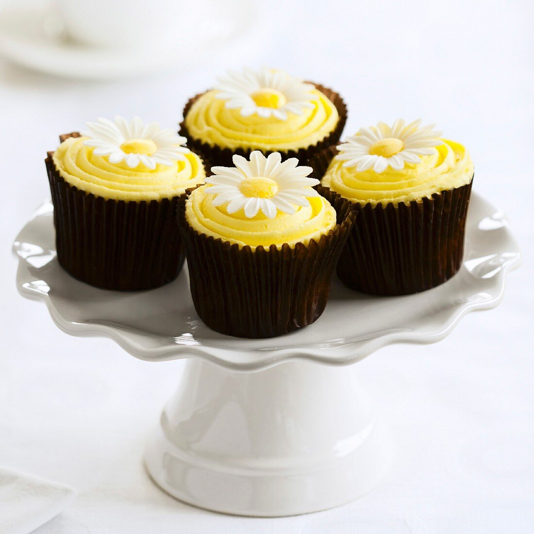 Gelbe Cupcakes, verziert mit Gänseblümchen, auf Kuchenständer