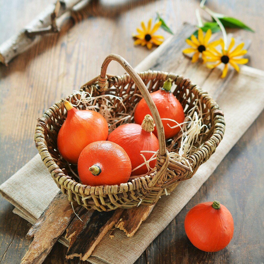 Small hokkaido pumpkins in a basket with flowers in background