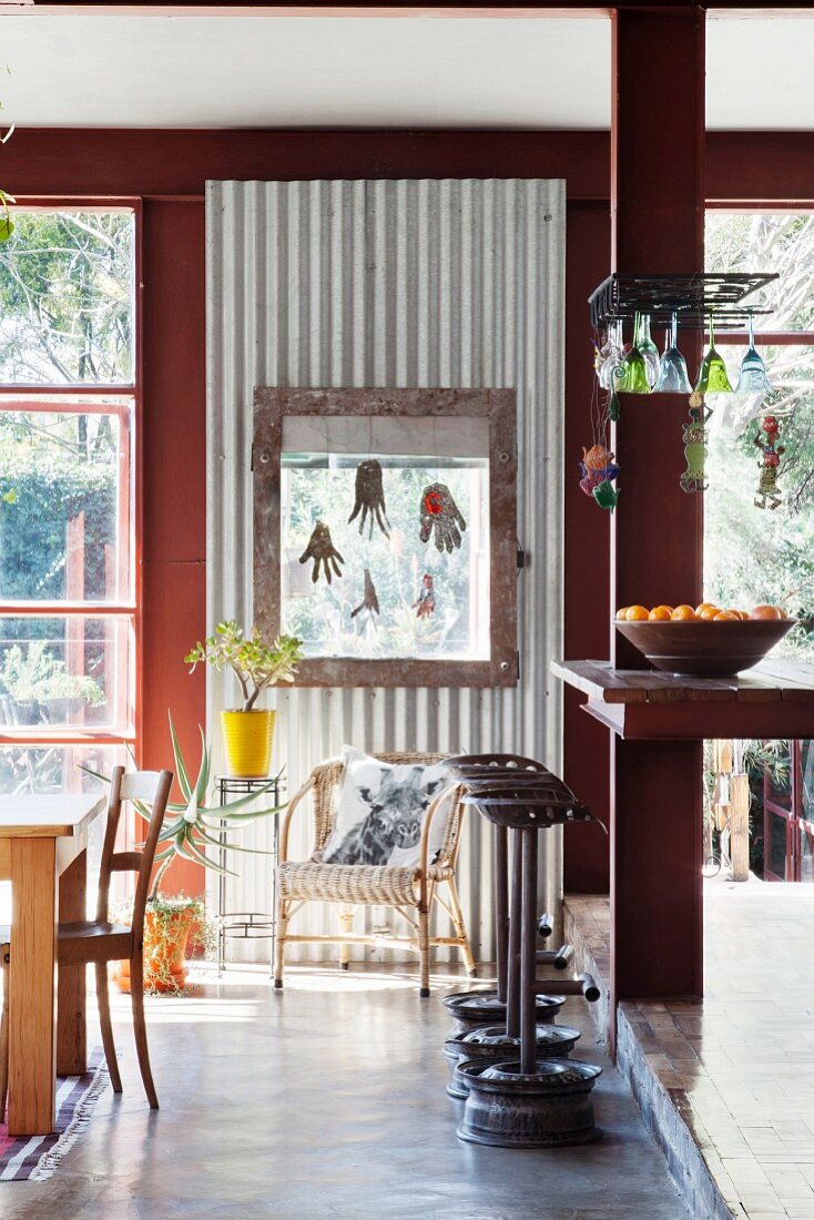 Kitchen counter and DIY bar stools made from reclaimed materials in front of corrugated steel panel between windows