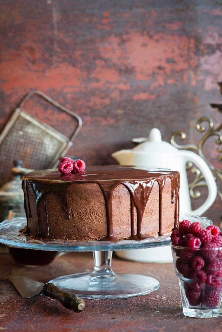 Schokoladenkuchen mit Schokoladenglasur und Himbeeren auf Tortenständer