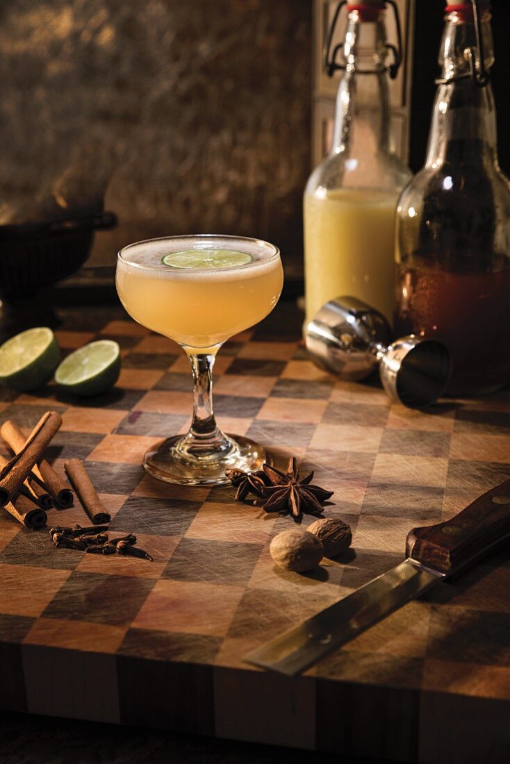 Würziger Ingwer-Cocktail mit Limettenscheibe, umgeben von Sternanis, Zimt, Gewürznelken und Muskatnuss