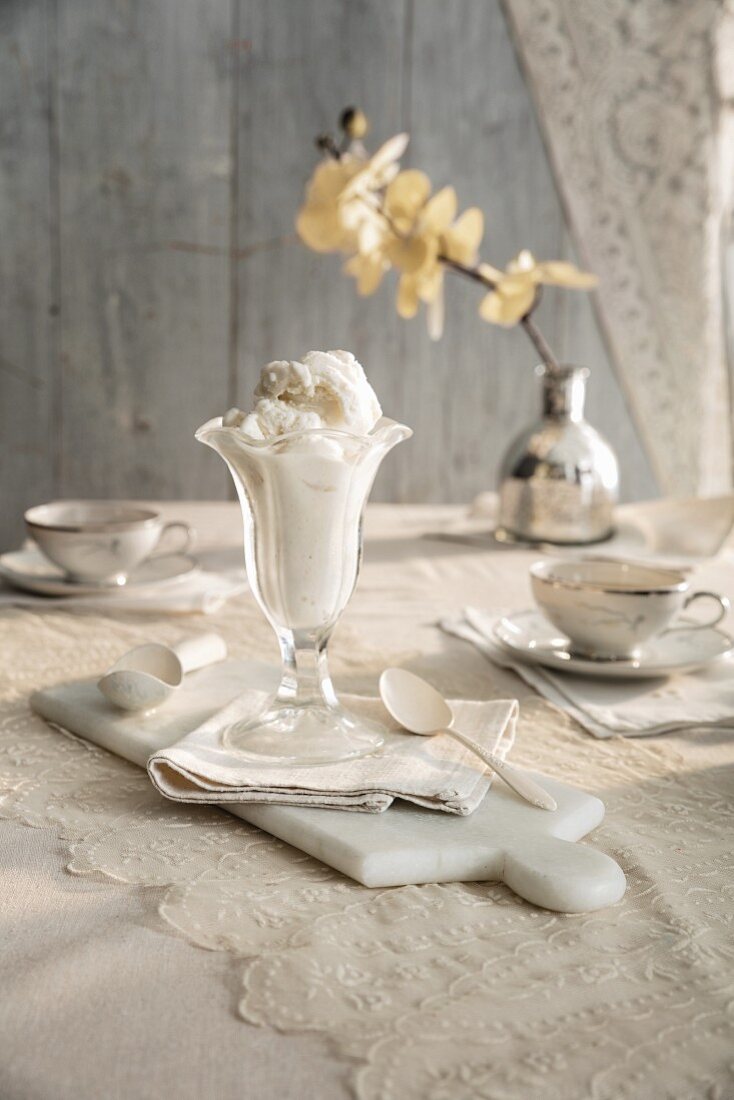 A vanila ice cream sundae on a vintage table with a lace tablecloth and white orchid