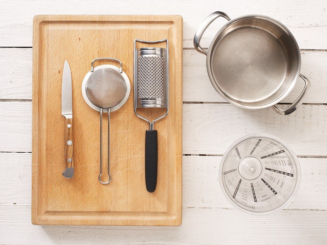 Verschiedene Küchenutensilien: Messer, Sieb, Reibe, Messbecher und Topf