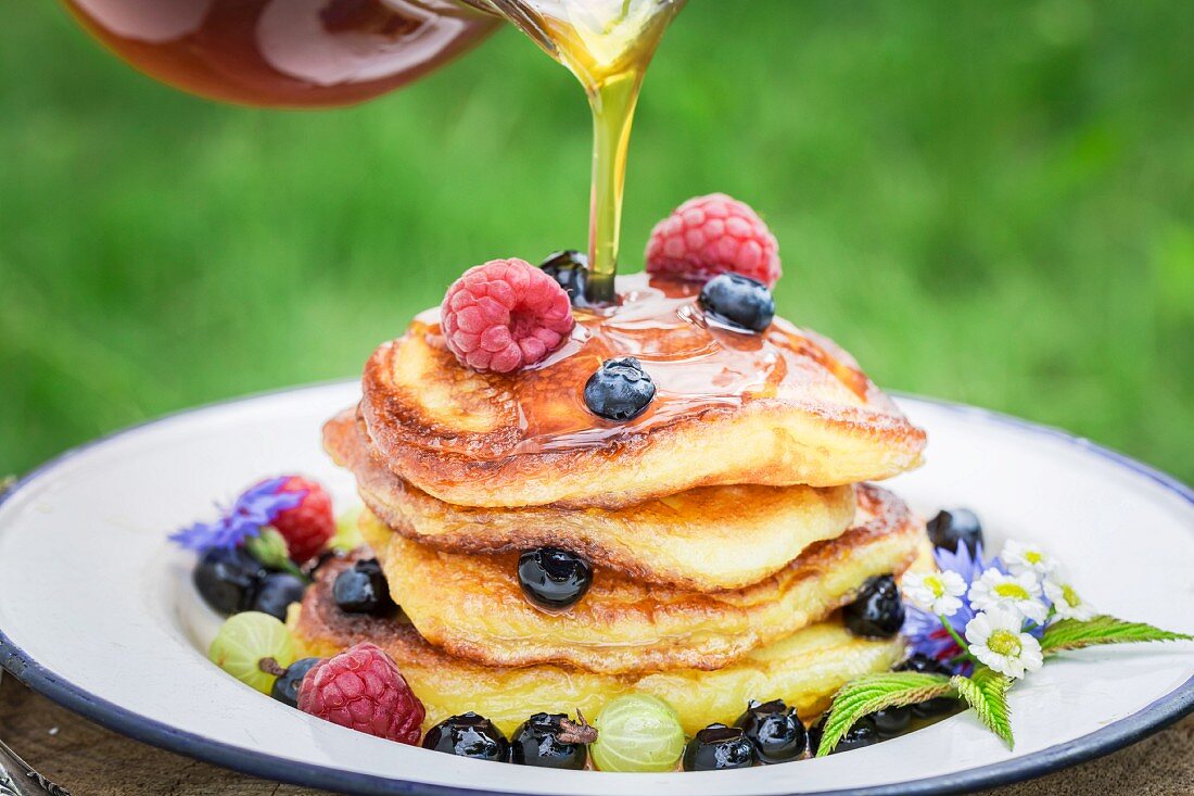 Maple syrup being drizzled onto a pile of pancakes with fresh berries