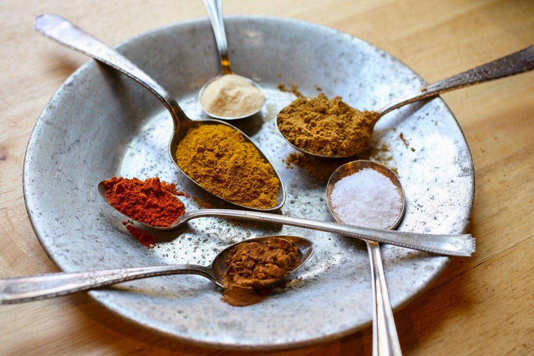 Several spoons containing spices on a metal plate