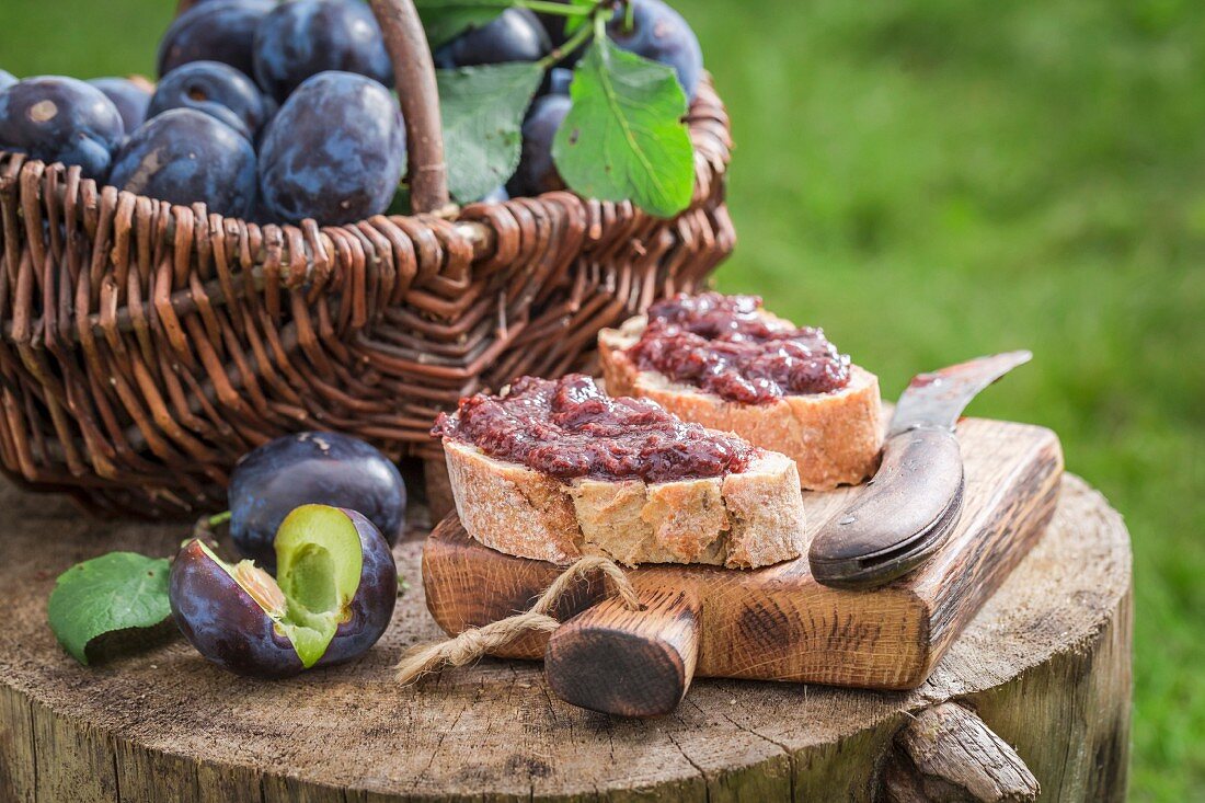 Bread topped with plum jar on a wooden board in the garden