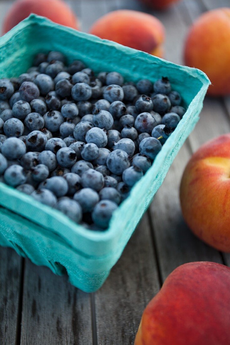 Blueberries in a cardboard punnet surrounded by peaches
