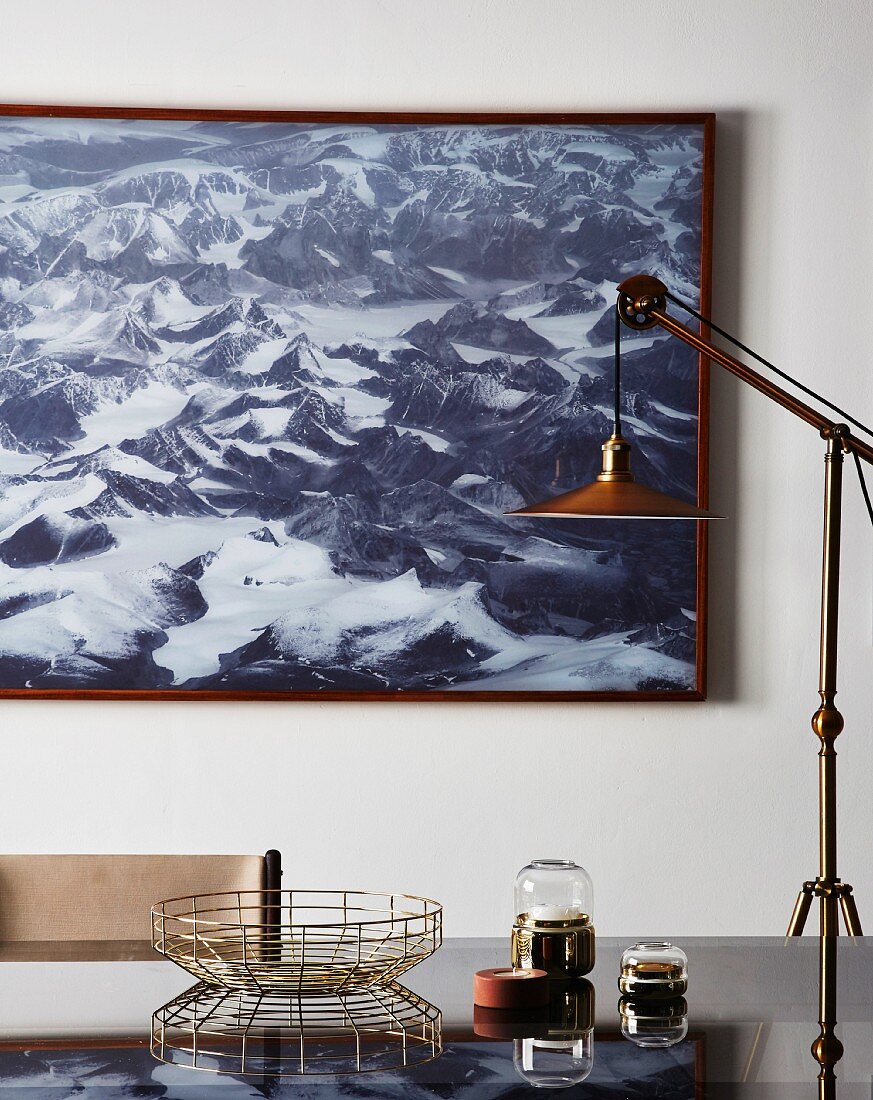 Standard lamp and ornaments on glass table in front of picture of mountains