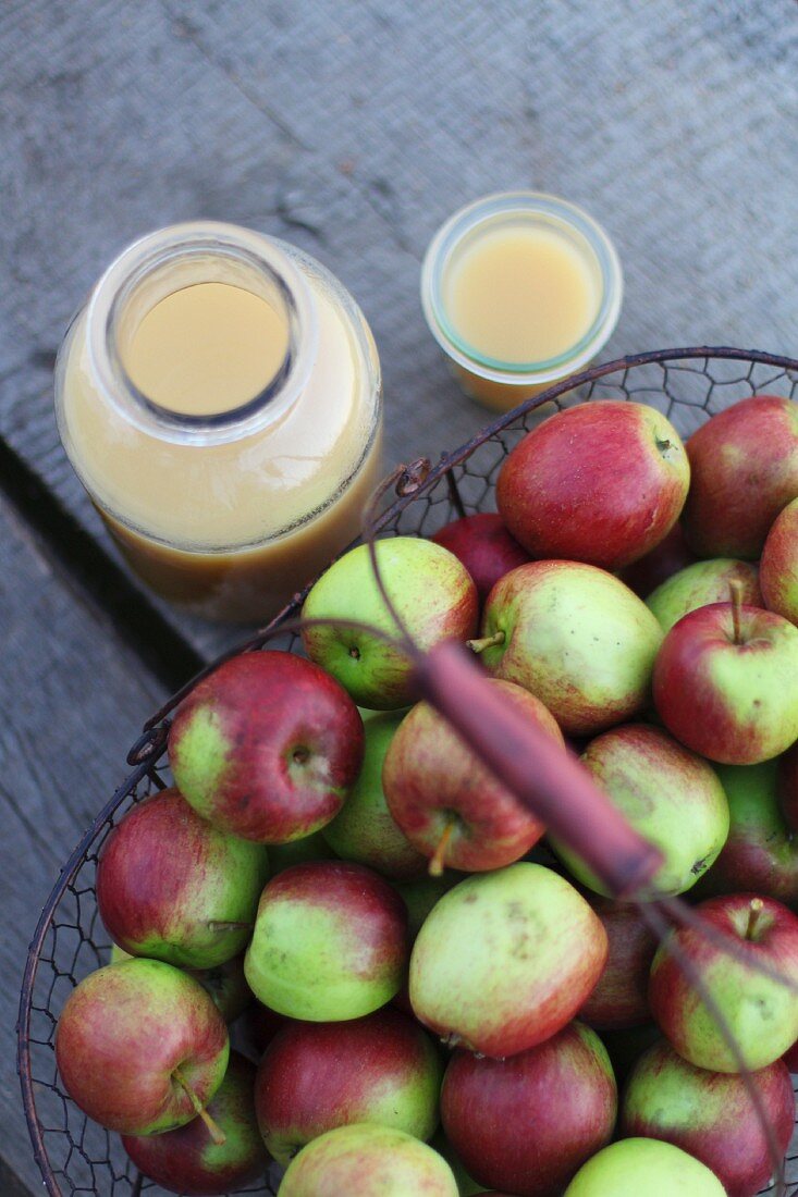 Frischer naturtrüber Apfelsaft in Glas und Flasche neben Korb mit Äpfeln
