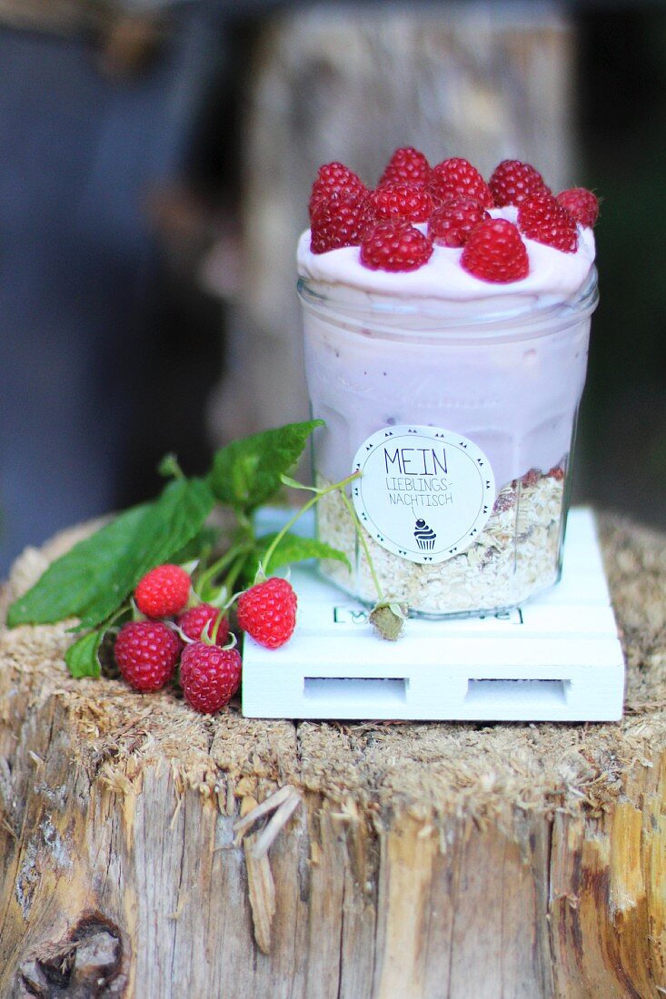 A layered dessert with muesli and raspberry cream in a preserving jar with a deocrative label
