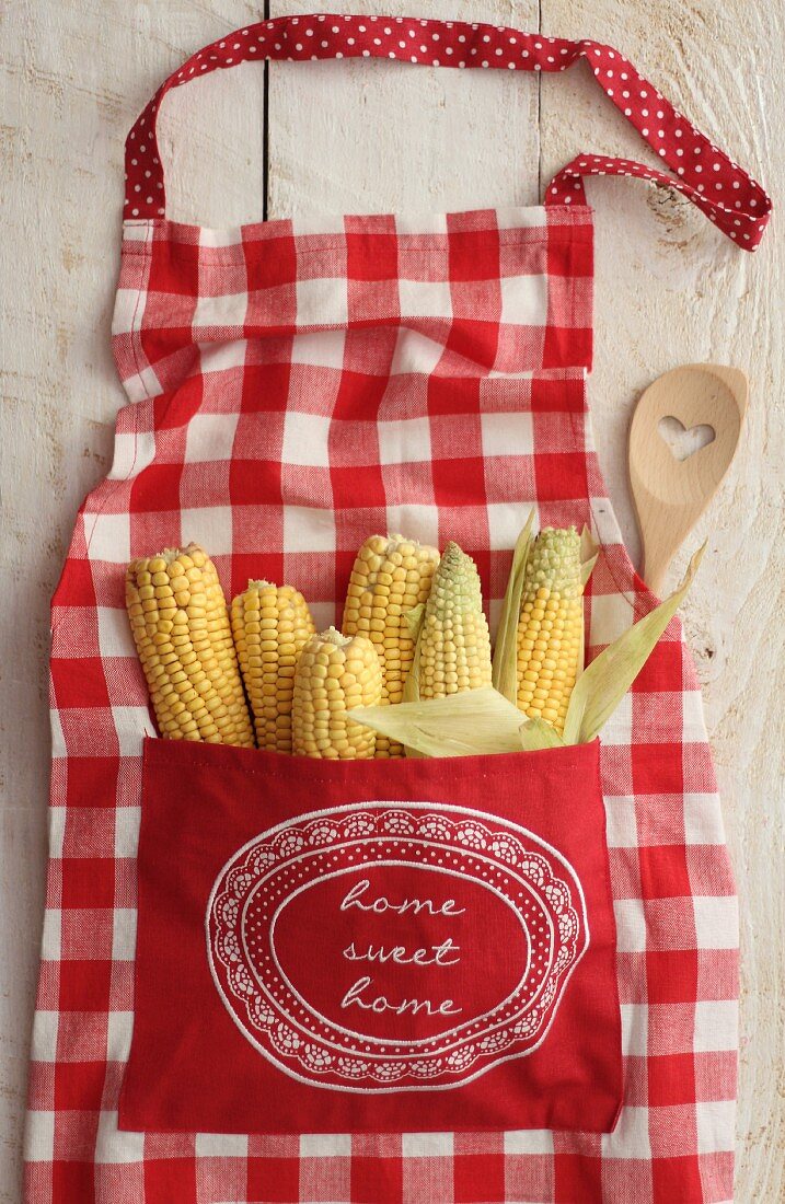 Sweetcorn in the pocket of a red and white checked apron