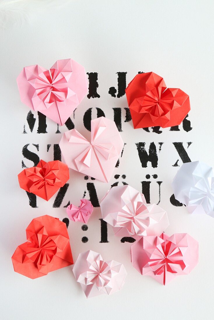 Origami hearts in pin and red on paper printed with letters