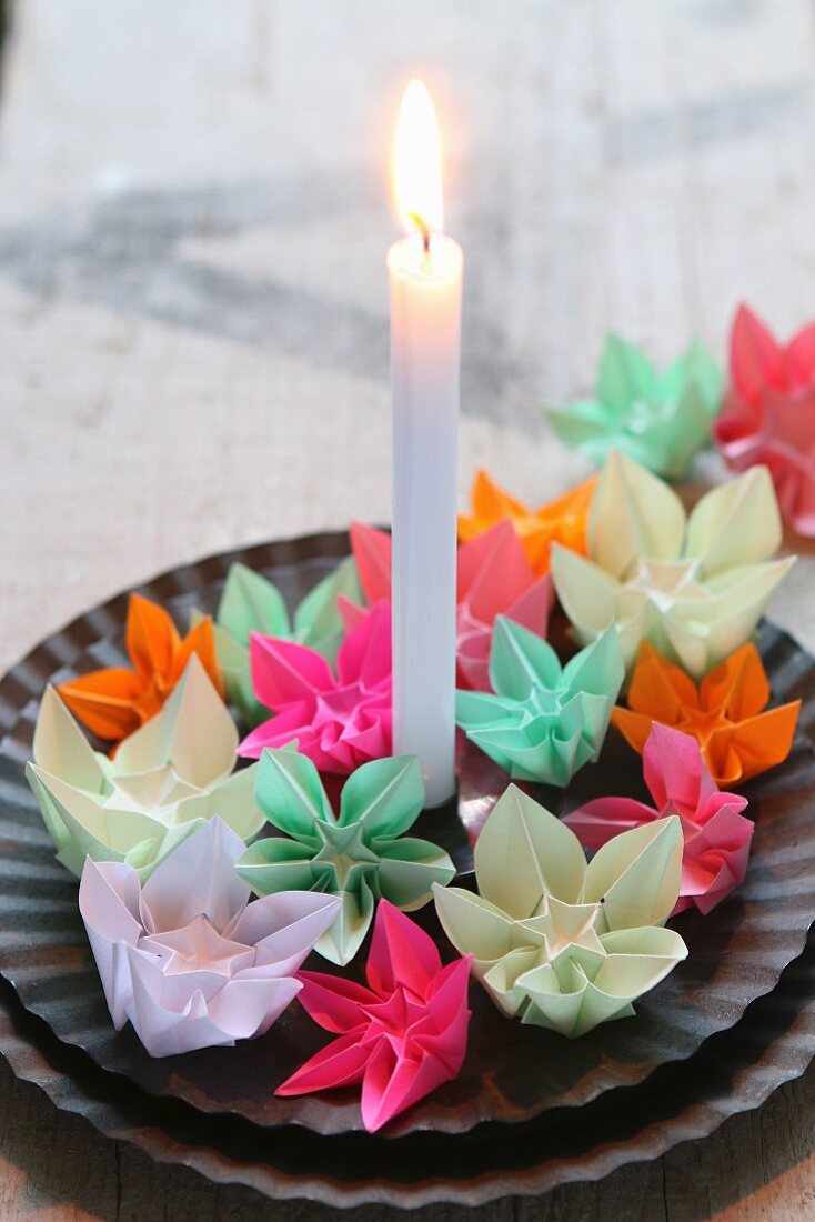 Colourful origami flowers and candle on black plates