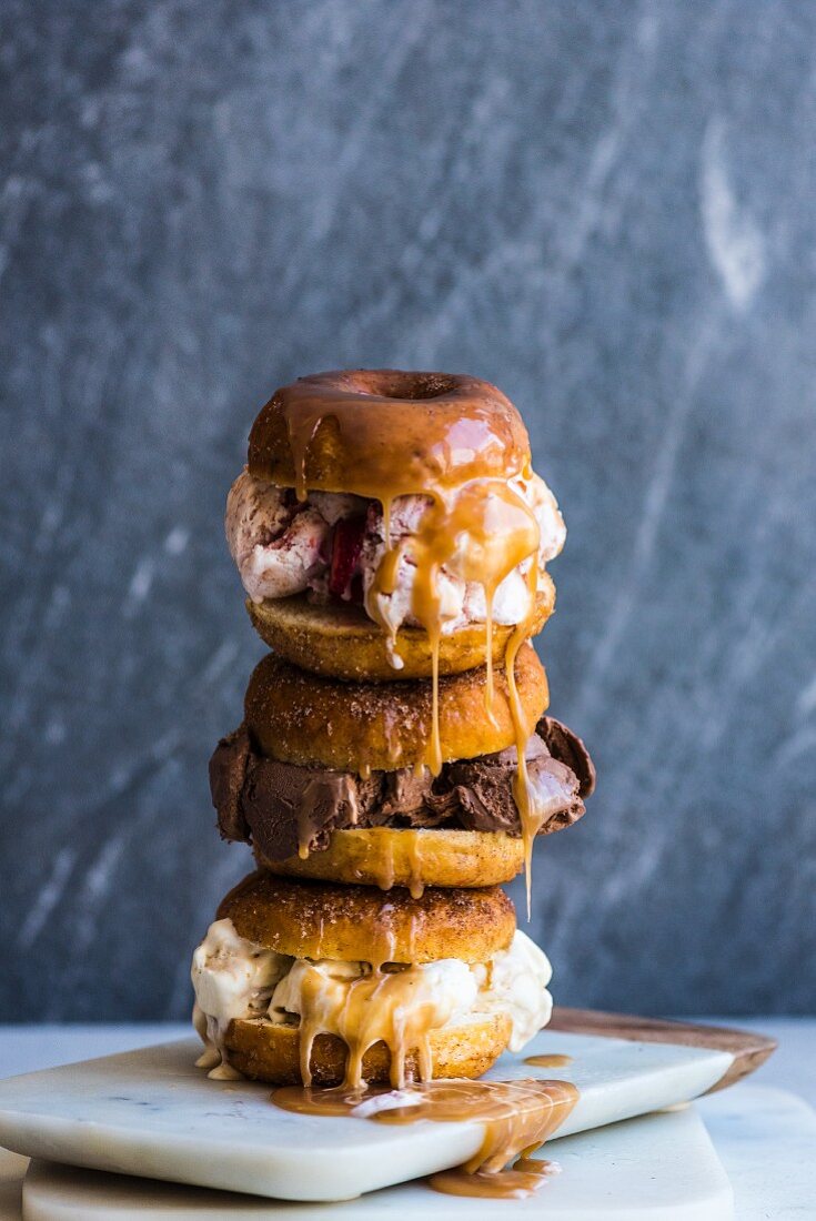 A stack of doughnut ice cream sandwiches with caramel sauce dripping down