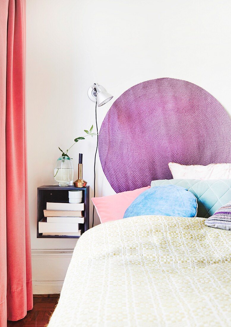 Round purple rug hung on wall above head of bed