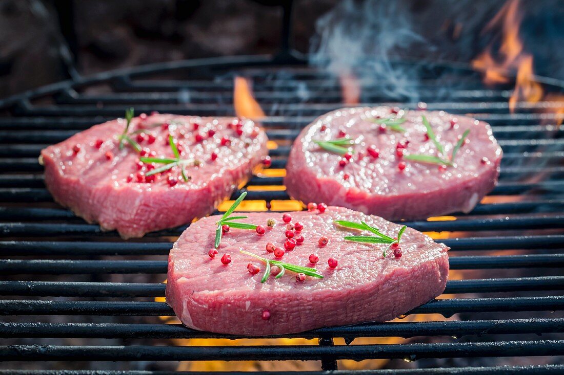 Frische Steaks mit Pfeffer und Rosmarin auf Grillrost mit Feuer