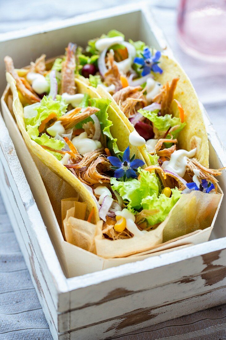 Tortillas filled with pulled pork, lLettuce and vegetables in a wooden crate