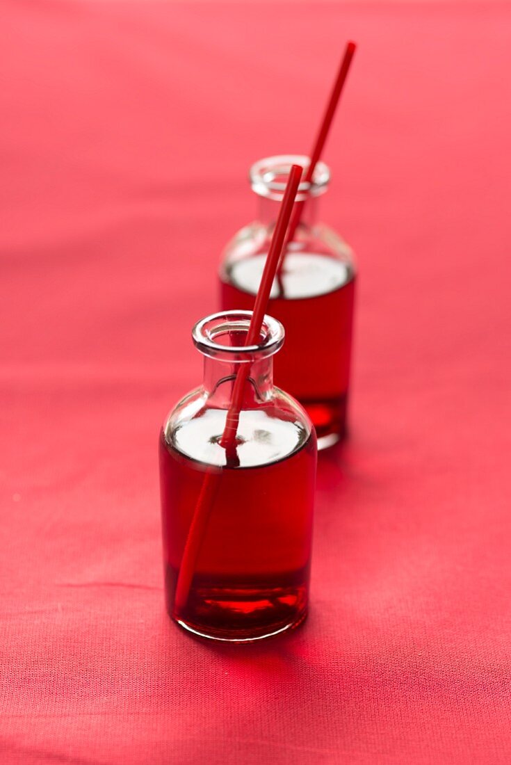 Cranberrysaft mit Strohhalmen in Glasfläschchen auf rotem Untergrund