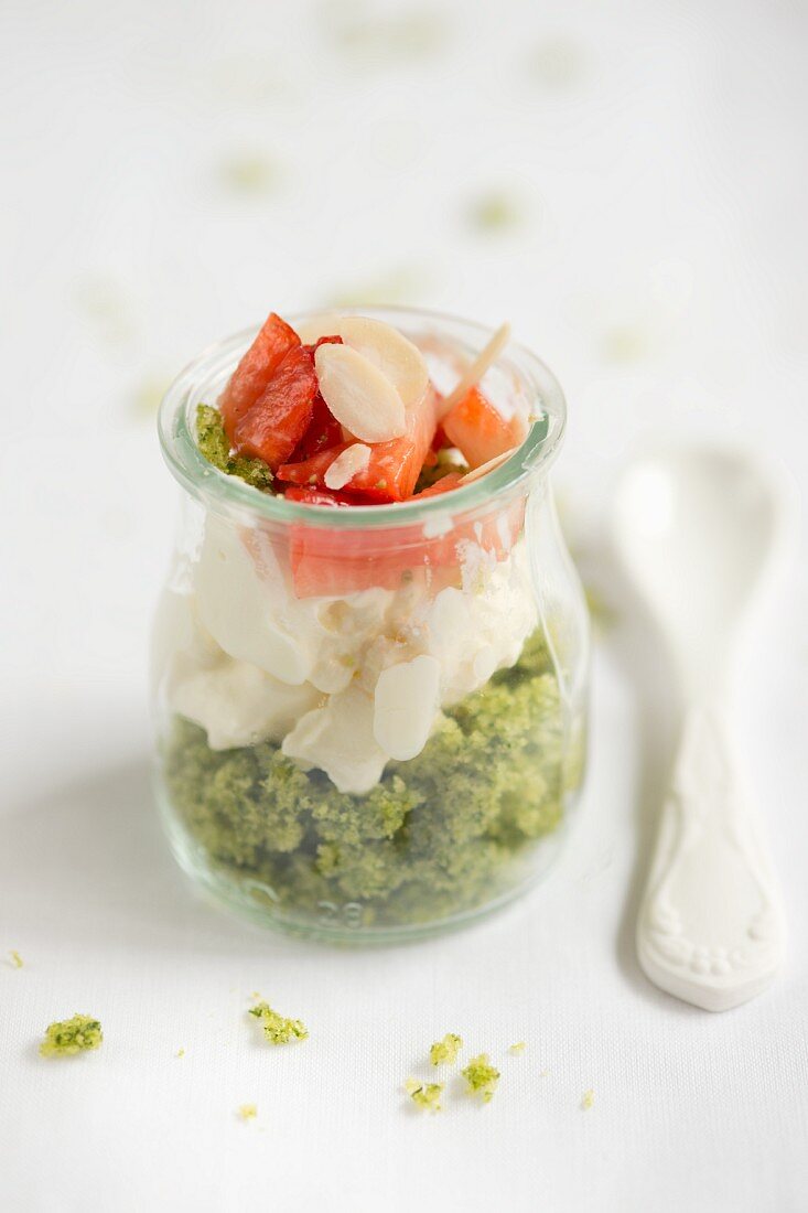 A layered cake dessert in a glass jar with spinach cake, cream and strawberries