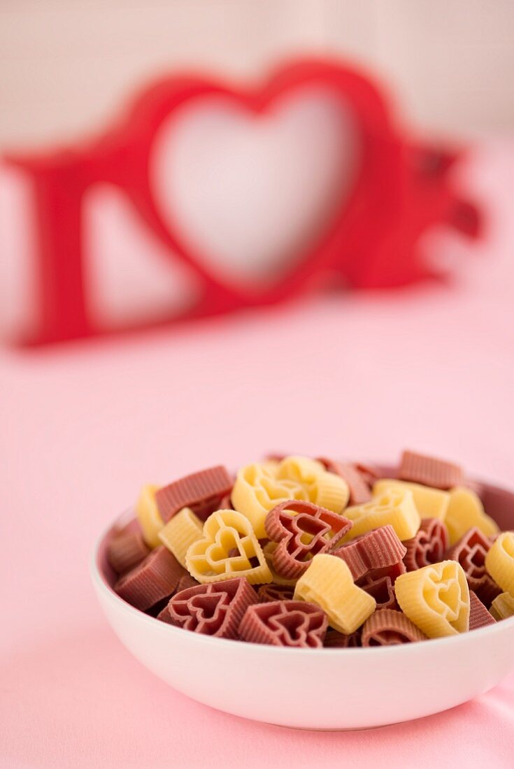 A bowl full of heart-shaped pasta with the word 'LOVE' in the background