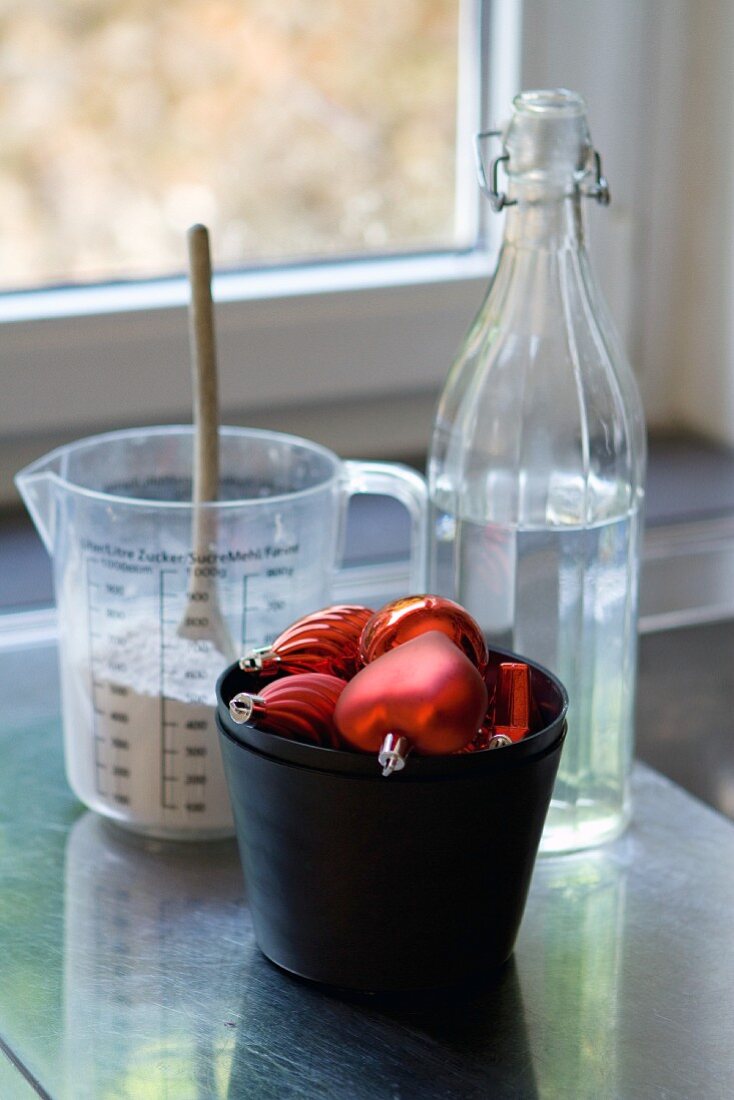 Red Christmas-tree bauble in front of jug of plaster and bottle of water