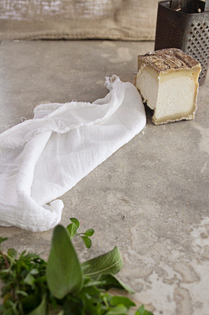 An arrangement of cheese, a cheesecloth, a grater and fresh herbs
