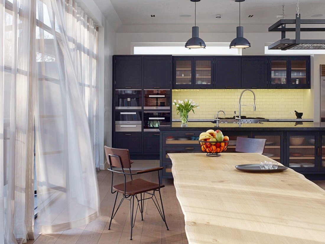 Blick über langen Esstisch aus Holz in die Küche im Industriestil
