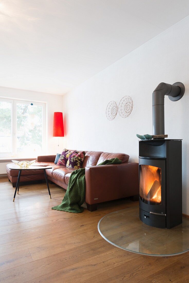 Lit fire in stove next to brown leather sofa