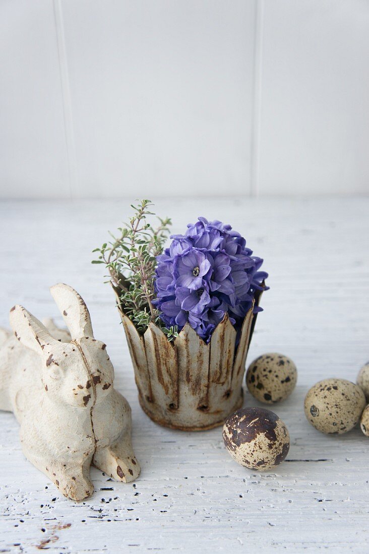 Osterhase neben Metallkrönchen mit Hyazinthen und Thymian