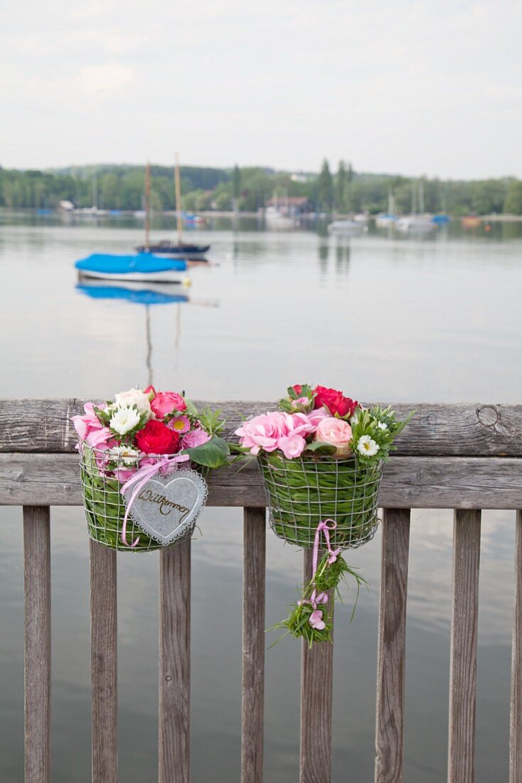 Zwei Metallkörbe mit Blumen und Gras am Geländer zum See