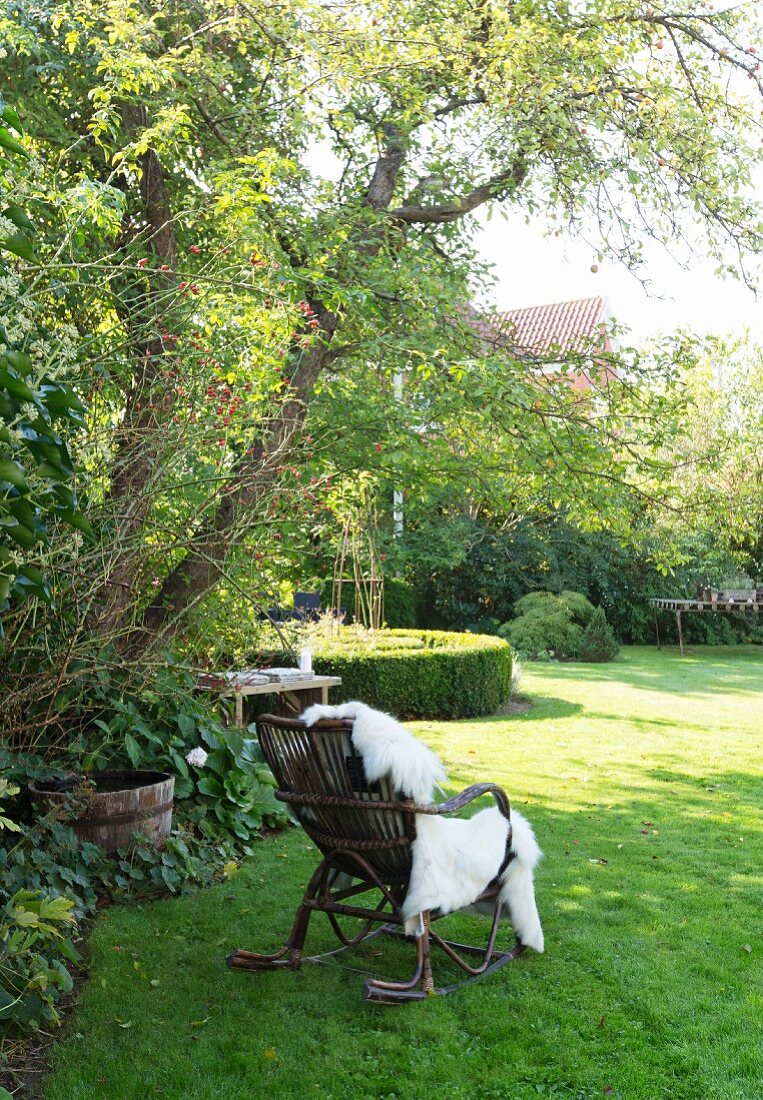 Schaukelstuhl aus Rattan mit einem Fell im Garten unterm Baum