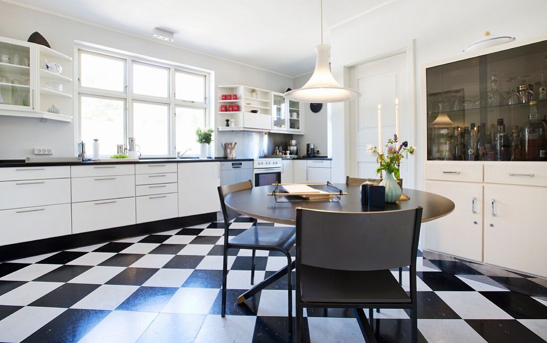 Round table on black and white chequered floor in white fitted kitchen