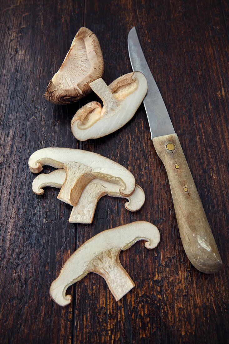 A sliced shiitake mushroom with a knife on a wooden surface