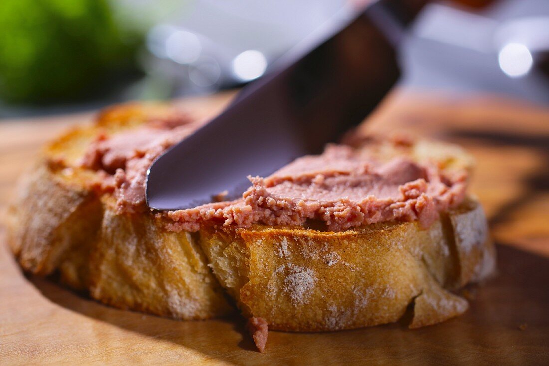 Liver pâté being spread on a slice of baguette