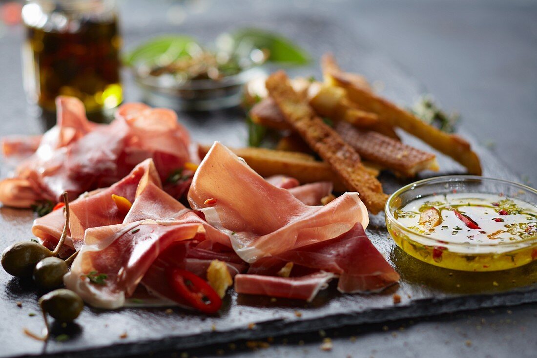 A starter platter with ham, breadsticks, olives and a dip