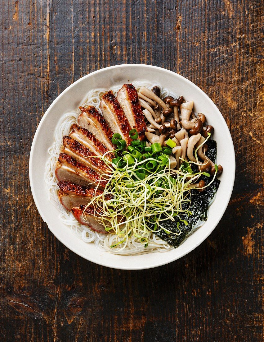 Rice noodles bowl with Peking Duck and mushrooms on wooden background
