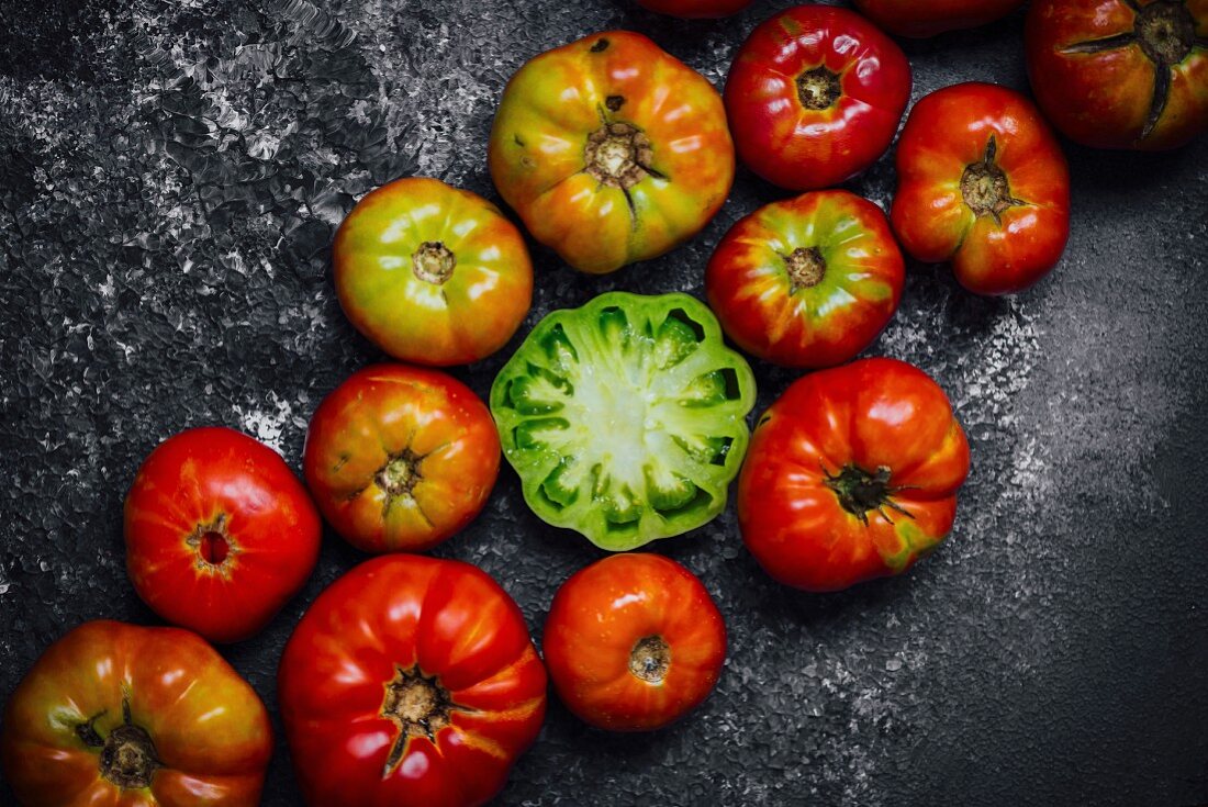 Ganze rote Heirloom-Tomaten und eine halbierte grüne Tomate auf schwarzem Untergrund