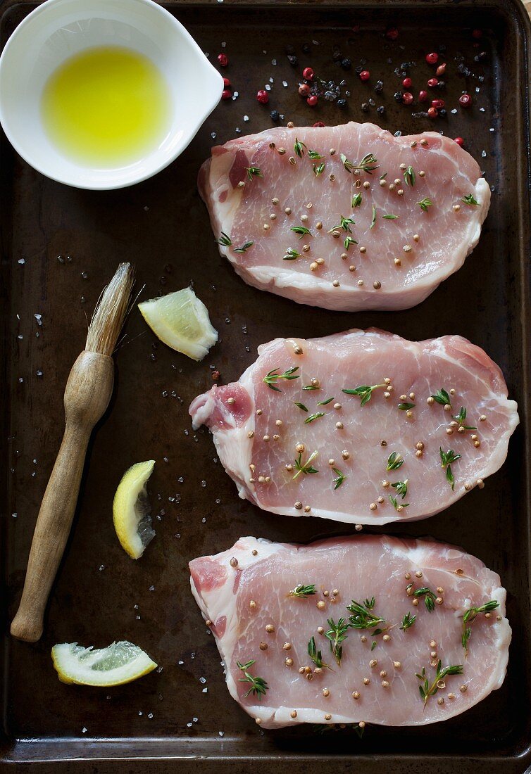 Drei rohe gewürzte Schweinekoteletts auf Ofenblech (Aufsicht)