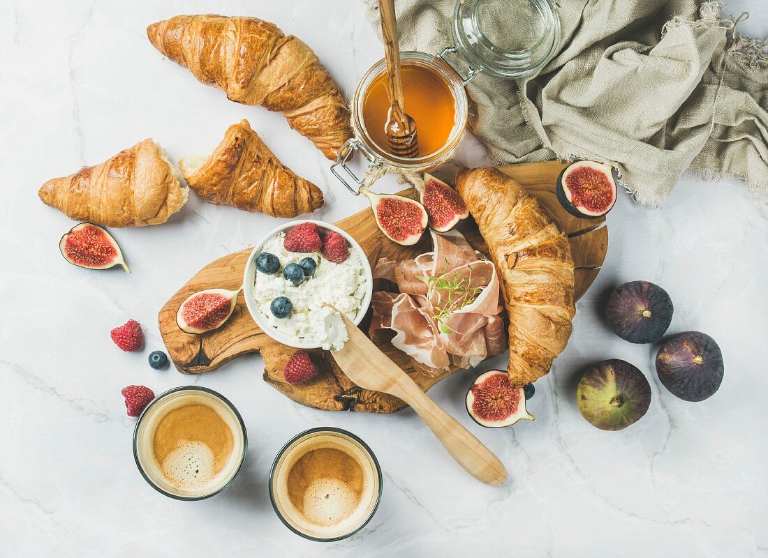 Frühstück mit Croissants, Ricotta, Feigen, Beeren, Schinken, Honig und Espresso