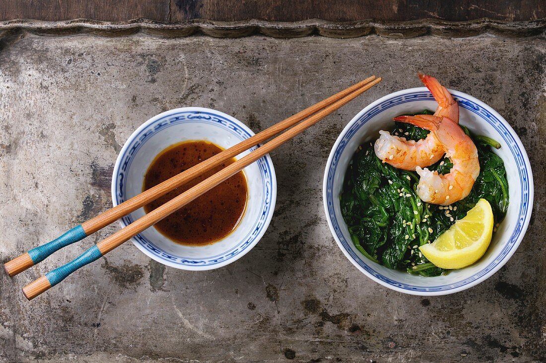 Spinach with pan-fried prawns, lemon and sesame seeds next to a bowl of soy sauce and chopsticks