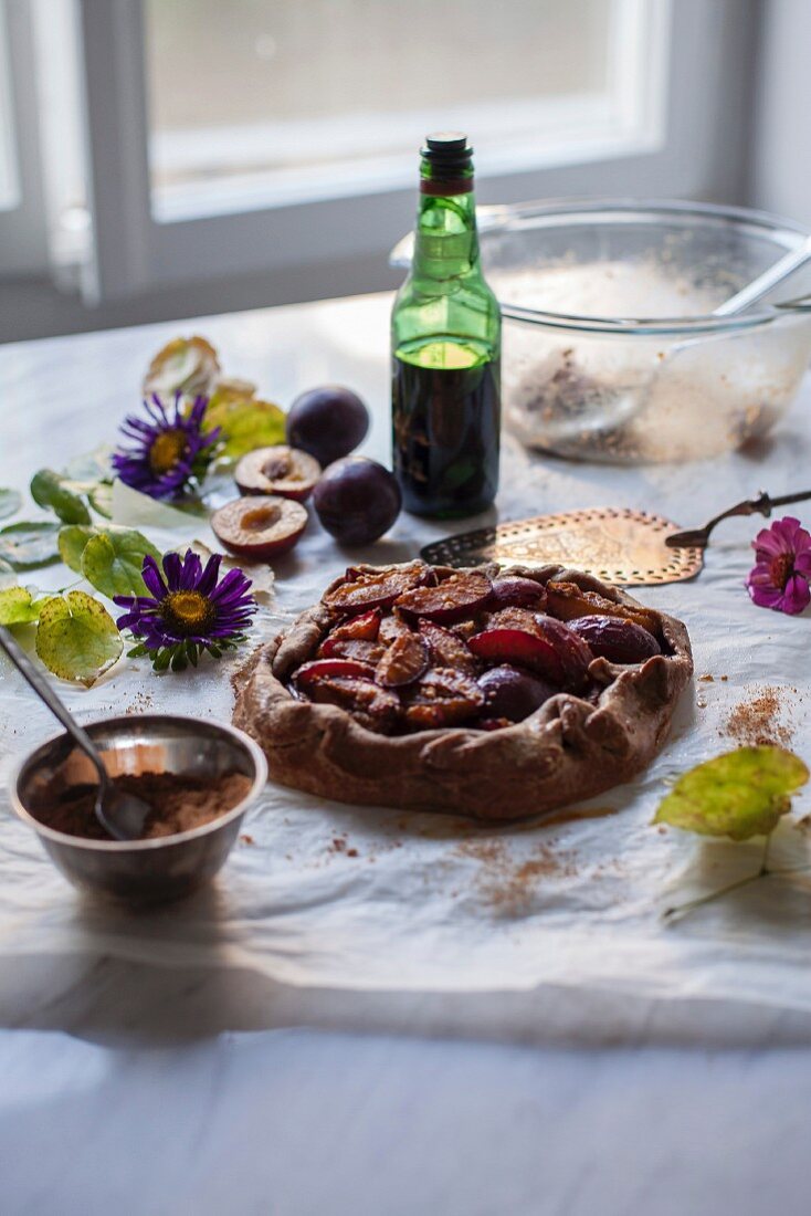 A plum galette with baking paper and a white marble table