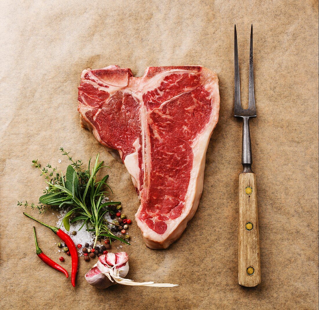 Rohes T-Bone-Steak, Gewürze und Fleischgabel auf Papier